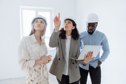 A diverse team of architects wearing helmets discusses interior plans with a laptop in a bright room.